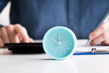 Businessman Calculating Invoice With Alarm Clock