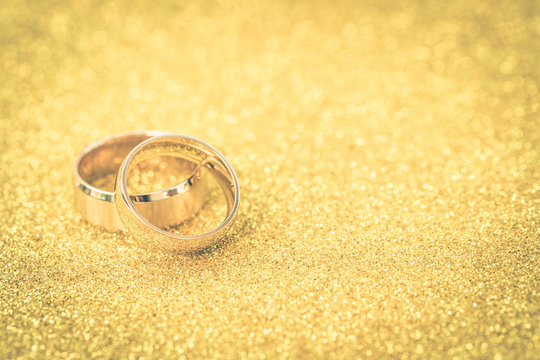 Gold wedding rings of bride and groom on gold gliter