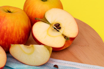 Whole and cut into pieces apples and protective mask lie on a round cutting board on a yellow background close up.Harvest coronavirus concept.The concept of food shortage due to the covid-19.