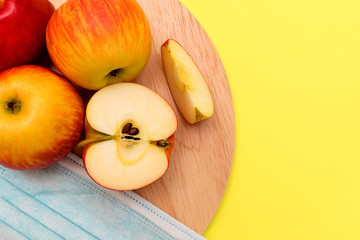 Whole and cut into pieces apples and protective mask lie on a round cutting board on a yellow background.Harvest coronavirus concept.The concept of food shortage due to the covid-19.