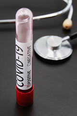 Conceptual photo. Blood test sample for presence of coronavirus and Stethoscope on dark background. Tube containing a blood sample that have tested positive for coronavirus. Closeup