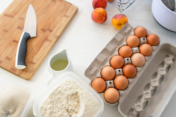 Peach cake recipe ingredients. Eggs, sugar, flour, vegetable oil, fresh peaches close up on white background, top view