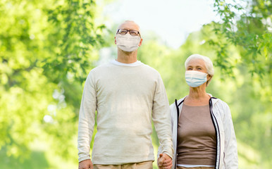 health, quarantine and pandemic concept - senior couple wearing protective medical mask for protection from virus holding hands outdoors over green natural background