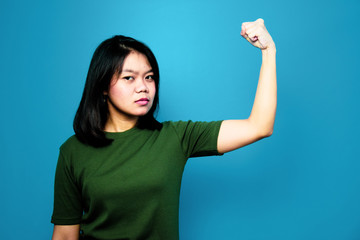 Portrait of Young beautiful asian women using Green T-shirt with blue isolated background, raises arms and shows biceps