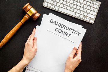 Bankruptcy court concept with document in hands and gavel on black background top-down