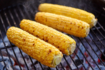 cooking, barbecue and food concept - close up of corn roasting on brazier grill outdoors
