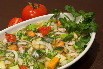 Healthy Italian vegetable minestrone soup with carrot, peas, corn, potatoes, zucchini, tomatoes and other vegetables in a white bowl.
