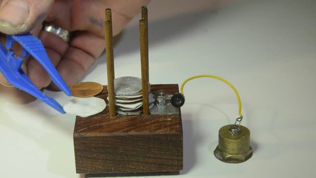 Assembly of a Voltage Column with plates of zinc, copper and electrolyte. Some elements have already been assembled. The column makes power for a LED light. Model of first battery discovered by Volta.