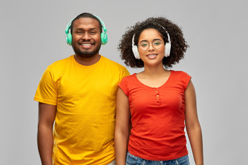 leisure, music and people concept - happy smiling african american couple with headphones over grey background