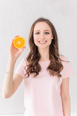 Attractive female in rose t-shirt holding orange fruit over white background