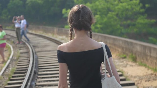 girl in black top walks along track on popular bridge towards tourists taking photos of wild nature slow motion backside view. Concept nature travel lifestyle