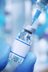 close up of blue rubber glove fingers holding a vaccine vial and syringe
