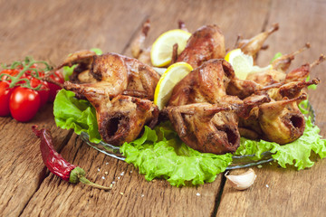 Dinner. Barbecue fried quail carcasses with on orange with tomatoes and fresh parsley and a glass of wine on a wooden table, top view