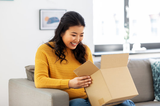 delivery, shipping and people concept - happy asian young woman with cardboard parcel box at home