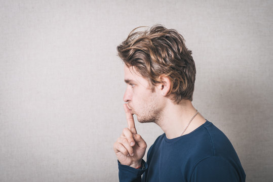 A man shows a finger to his mouth quiet. On a gray background.