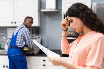 Frustrated Woman Looking At Bill On Clipboard In Kitchen