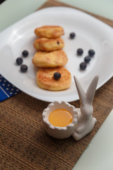 Syrniki or cottage cheese pancakes with blueberries and honey on white plate with blue napkin on kitchen table. Healthy breakfast, diet concept.