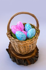 Easter eggs in wicker basket on wood background. White background. Pink and blue on the green grass. Easter concept