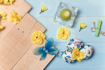 Decorated Easter eggs, yellow flowers, burning candle on wooden blue boards background. Spring and Easter concept. Copy space.