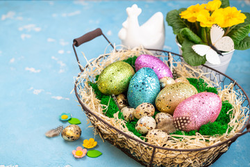 Spring Easter background for spring holidays. Easter composition with colorful Easter eggs on moss in basket, chicken bird and spring flower pot. Top view