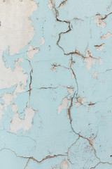 Texture of cracked wall with light blue paint, background or backdrop of abandoned building exterior.