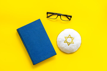 Jewish Kippah Yarmulkes hats with Star of David on Prayer book on yellow background top view