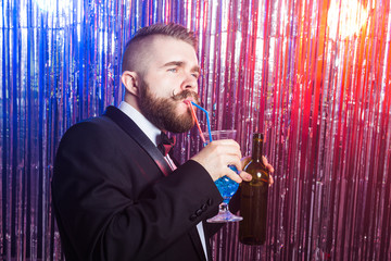 Club party and holidays concept - Portrait of elegant handsome man in a expensive suit holds blue cocktail on shiny background.