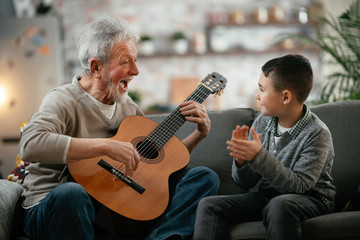 Grandpa and grandson playing guitar. Grandfather and grandson enjoying at home.	