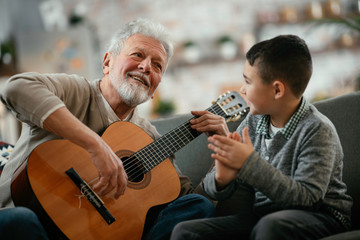 Grandpa and grandson playing guitar. Grandfather and grandson enjoying at home.	