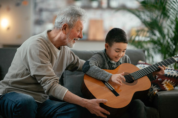 Fototapeta premium Grandpa and grandson playing guitar. Grandfather and grandson enjoying at home. 