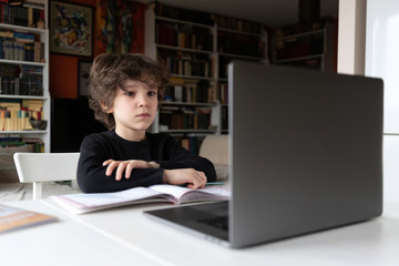 Indoor life at the coronavirus quarantine. Cute curly boy has school lesson online.