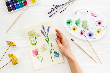 Painting. Female hands draw flowers on white background top-down