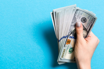 Top view of female hand holding a pack of one hundred dollar bills on colorful background. Wage and...