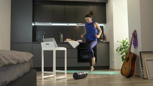 Fit woman doing sport fitness exercises online using app on laptop computer at home during coronavirus quarantine. Female having online aerobic fitness courses while staying at home. Workout at home