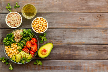 Quinoa, avocado and chickpeas in bowl in hands - balanced healthy food - on wooden table. Top view copy space