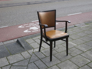 lonely black painted chair with brown upholstery on an abadoned sidewalk