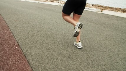 Legs of female athlete jogging along seaside road. Woman in sportswear and sneakers running outdoors. Tracking, vertical motion, zoom in, closeup. Sport concept - Powered by Adobe
