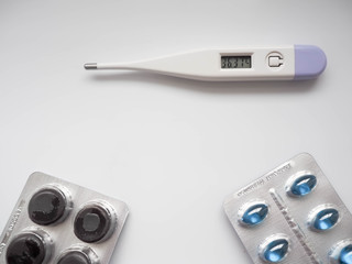 White ternometer with normal temperature below two packs of blue and black tablets on a light...