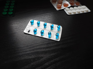 Blue pills in a pack with one empty cell on a dark background with other levarst plates