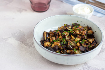 Plate of fried diced eggplants and creme fraiche on grey background. Ready to eat.