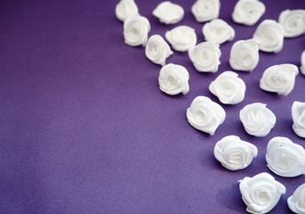 A lot of little white satin roses laid diagonally on a purple background