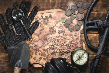 Metal detector, old treasure map and old coins on wooden flat lay table background.