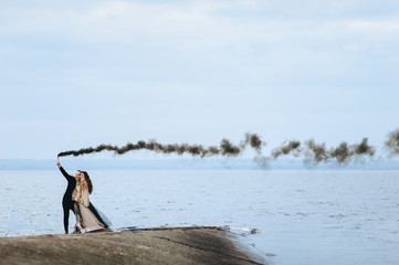 Stylish newlyweds hug and hold a pyrotechnic device with black smoke against the background of the...