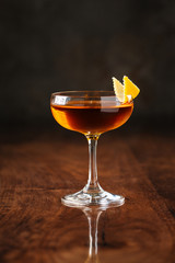 delicious dark cocktail in margarita glass with orange peel on the dark wooden background, side view, vertical