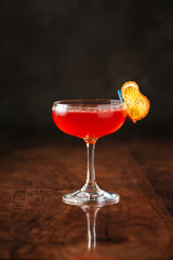 delicious red fruit cocktail in margarita glass with dry orange slice on the dark wooden background, side view, vertical