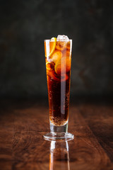 fresh cool delicious long island cocktail with ice, tea and alcohol on the dark wooden background, side view, vertical