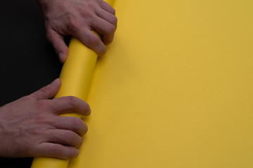 Hands roll yellow paper on a black background. Minimalism. Diagonal line. Matte black. Dark mode...