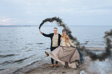 Stylish newlyweds hug and hold a pyrotechnic device with black smoke against the background of the...