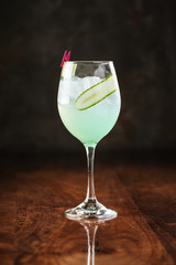 fresh aquamarine cocktail in a wine glass with ice and cucumber on the dark wooden background, side view, vertical