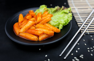 Spicy Tteokbokki on black crockery with metal chopstics.